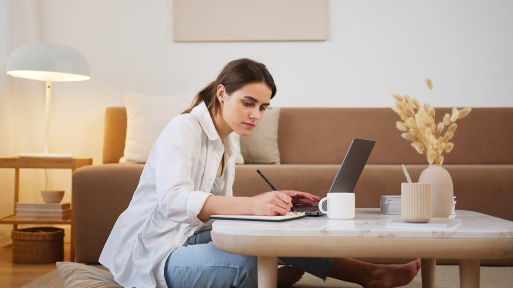 Woman writing notes in front of laptop